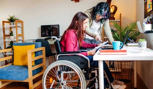 young woman in wheelchair looking at paperwork with friend